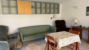 A living room with a green sofa, two armchairs, a wooden table with a tablecloth, a lamp, and a cabinet with glass doors. - L'Aminèxe - simple quiet under the stars in the fresh air (Tourrettes-sur-Loup)