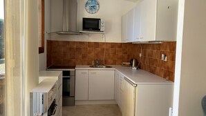 A compact kitchen with white cabinets, a microwave, and a clock on the wall. - L'Aminèxe - simple quiet under the stars in the fresh air (Tourrettes-sur-Loup)