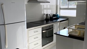 A modern kitchen with white cabinetry, a stainless steel range hood, a built-in oven, and a window providing natural light.