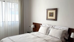A neatly made bed with white linens and a picture frame on the wall.