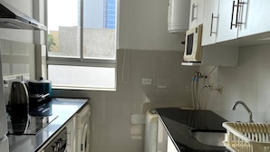 A modern kitchen with white cabinets, a black countertop, a built-in oven, and a window providing natural light.