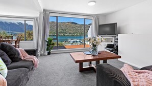 A modern living room with a large window offering a scenic view of mountains and a lake.
