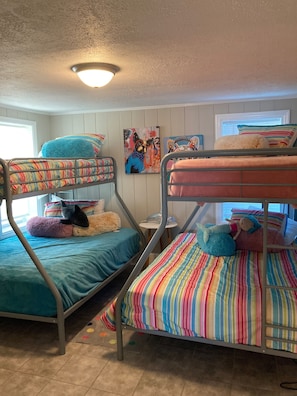 A bunk bed room with two beds, each with colorful bedding and pillows. There is a ceiling light fixture above the beds, and a window with blinds to the left. - 2nd Row 2 bed/1 bath Beach and Inlet property. Pet friendly with fee.  (Murrells Inlet)