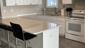 Eine moderne Küche mit weißen Schränken, einer großen Kücheninsel mit Barhocker, einem eingebauten Backofen und einem Fenster über der Spüle.