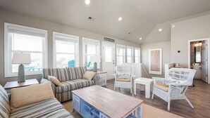 Un salon spacieux avec des canapés à rayures, une table basse en bois et des fauteuils en osier blancs.