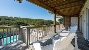 Une terrasse en bois avec des fauteuils Adirondack blancs, une piscine et une vue sur une zone boisée.