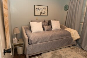 A bedroom with a bed, a bedside table with a lamp, a trash bin, a clock on the wall, and a window with curtains. - 2 Bedroom Oasis! Mother in-Law Apt Forest Lake, MN (Forest Lake)