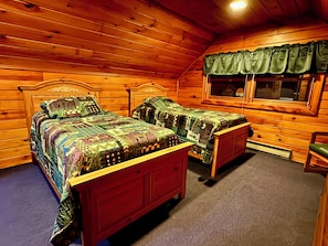 A wooden cabin bedroom with two beds, a window with curtains, and a small chair. - Chalet Cabin,  Gore Skiing, Pool, AC, Spacious Cabin, Loon Lake (Chestertown)