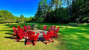 A circular arrangement of red Adirondack chairs around a central fire pit in a grassy outdoor area with trees in the background. - Chalet Cabin,  Gore Skiing, Pool, AC, Spacious Cabin, Loon Lake (Chestertown)