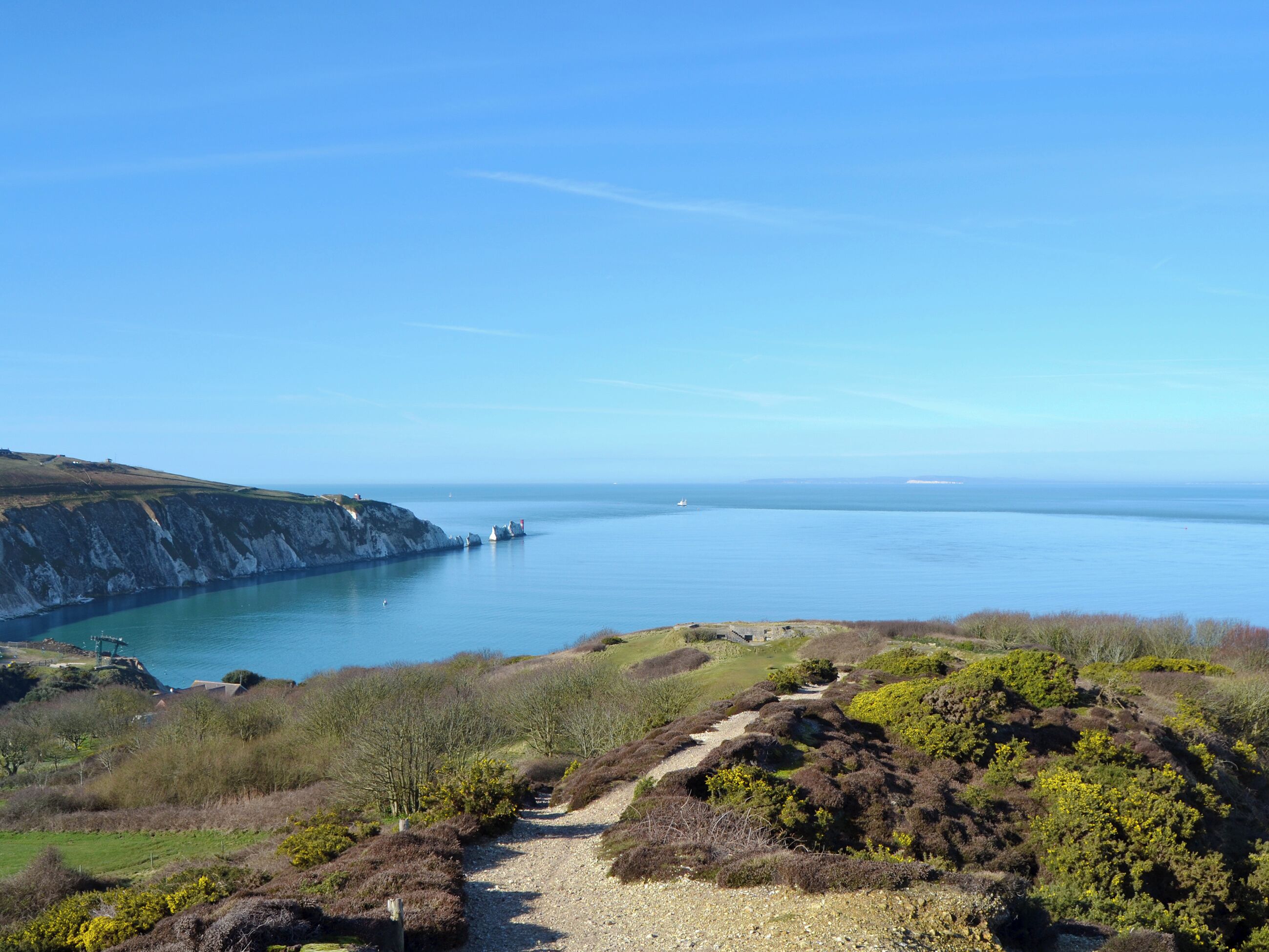 A coastal landscape with a clear sky, a rocky cliff, and a calm sea.