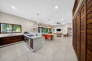 A modern kitchen with a central island, dining area with chairs, and a wooden wall.