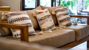 Un salon chaleureux avec un canapé, des coussins et une fenêtre donnant sur un paysage verdoyant.