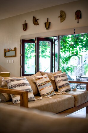 A cozy living room with a sofa, pillows, and a window with a view of greenery.