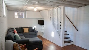 Un salon moderne avec un canapé gris, un fauteuil à motifs et un escalier doté de rampes blanches.