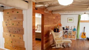 Une pièce avec un mur d’escalade en bois, une chaise blanche, une guitare et une bibliothèque remplie de jouets.