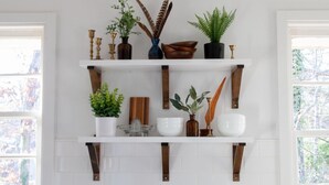 Une cuisine avec des armoires blanches et deux étagères blanches. Les étagères contiennent divers objets de cuisine, notamment une plante, un vase et un bol.