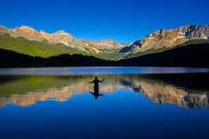 Una persona pescando en un lago tranquilo con montañas al fondo.