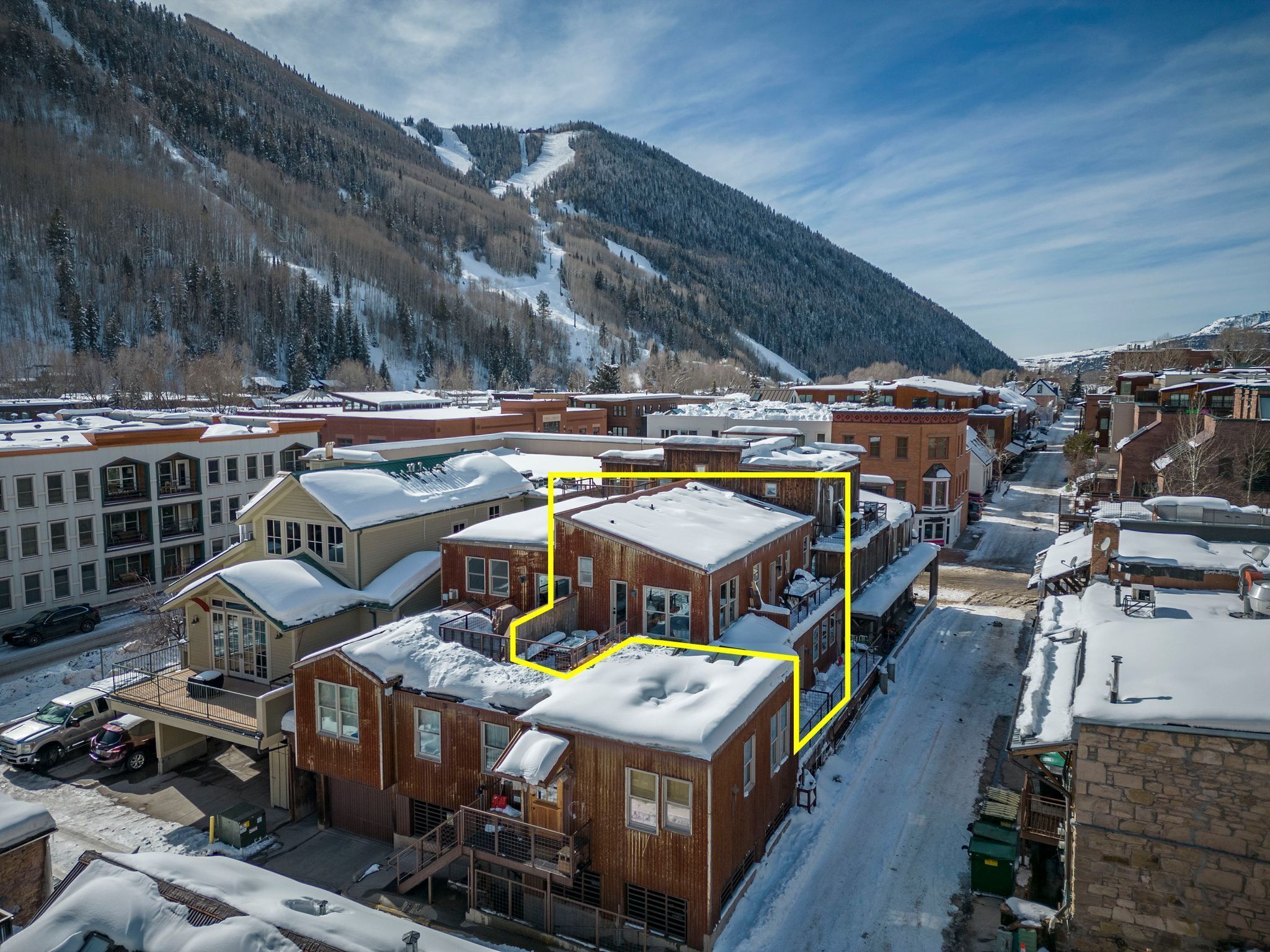 Une ville enneigée où se côtoient des bâtiments modernes et traditionnels, avec notamment un quartier remarquable qui comprend un bâtiment en briques rouges et un bâtiment blanc doté d’un balcon.