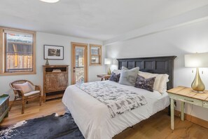Un dormitorio con una cama grande, una mesita de noche de madera, un sillón de mimbre y un aparador rústico.