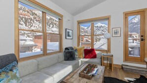 Un salon confortable avec un canapé, une table basse et de grandes fenêtres donnant sur une vue imprenable sur les montagnes.