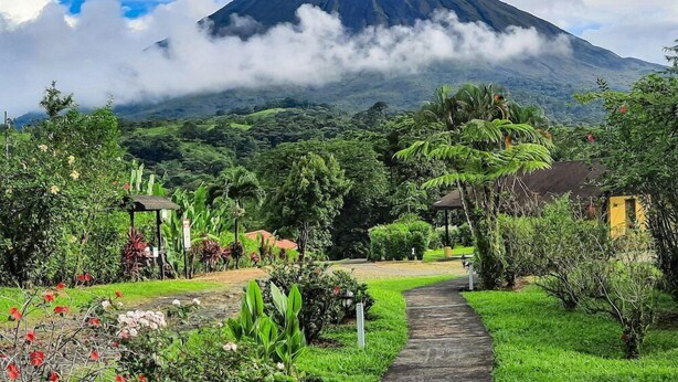 A pathway leading to a mountain with a lush garden and a small structure. - Campo Verde (La Fortuna)