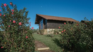 A wooden cabin with a sloped roof, surrounded by lush greenery and red flowers. - Campo Verde (La Fortuna)