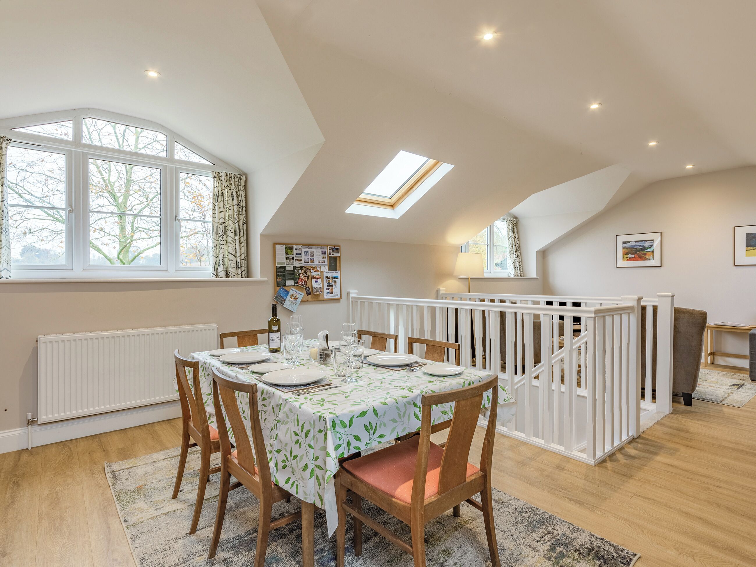 A dining area with a table set for four, a white railing, and a view of trees outside.