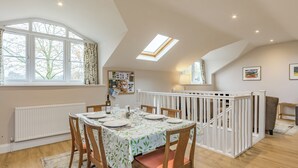 Un coin repas avec une table dressée pour quatre personnes, une rambarde blanche et une vue sur les arbres à l’extérieur.