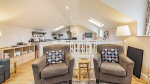 Un appartement-loft spacieux avec de hauts plafonds, une cuisine équipée d’appareils modernes, un coin repas et deux fauteuils agrémentés de coussins à motifs.