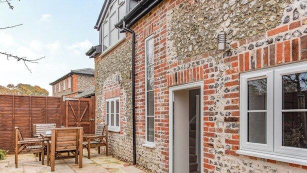 Une maison en pierre avec une terrasse en bois, une porte donnant sur un escalier et une fenêtre.