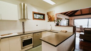 Una cucina moderna con mobili bianchi, un'isola centrale, forno integrato e una finestra che si affaccia sulla sala da pranzo.