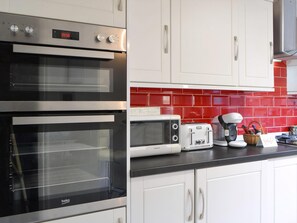 A kitchen with two ovens, a toaster, a coffee maker, and a red-tiled backsplash.