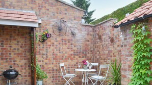 A brick patio with a grill, white folding chairs, and potted plants. - 2 bedroom accommodation in North Cave (North Cave)