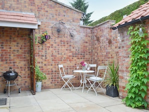 A brick patio with a grill, white folding chairs, and potted plants.