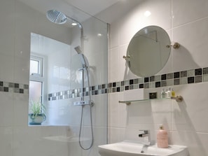 A modern bathroom with a glass-enclosed shower, a round mirror, and a white sink with toiletries.