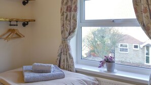 A bedroom with a bed, a window with curtains, a radiator, a plant, and wooden hangers on a wall. - 2 bedroom accommodation in North Cave (North Cave)
