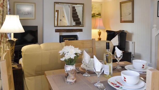 A hotel room with a sofa, a dining table set with plates, glasses, and a bottle, and a TV on the wall. - 2 bedroom accommodation in North Cave (North Cave)