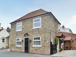 A two-story stone house with a black front door, white-framed windows, and a brick roof.