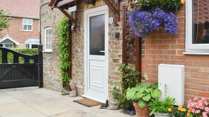 A brick cottage with a white door, a wooden porch, and hanging flower baskets. - 2 bedroom accommodation in North Cave (North Cave)