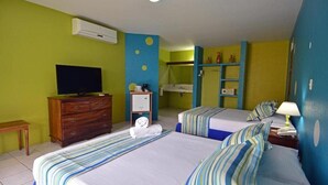 Habitación de hotel con dos camas, un televisor, un aparador y un baño con ducha y repisas con artículos de aseo.
