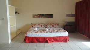Un dormitorio con cama, armario, un cuadro y una ventana con cortinas.