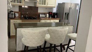 A kitchen with a central island, two upholstered bar stools, a stainless steel refrigerator, and a built-in oven.