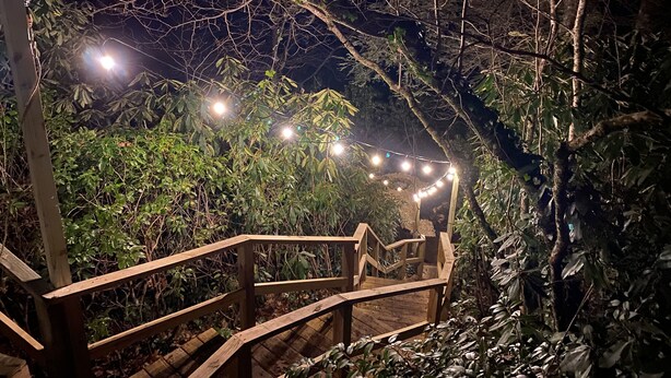 Eine Holztreppe führt zu einem überdachten Bereich mit Lichterketten.