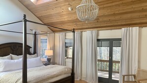 Ein Bett mit Baldachin, ein Holzkopfende, ein Chandelier und Blick ins Freie durch eine Glastür.