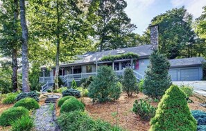 A two-story house with a covered porch, a stone chimney, and a well-maintained garden with various shrubs and a small water feature. - Sky Light. Walk to downtown Highlands (Highlands)