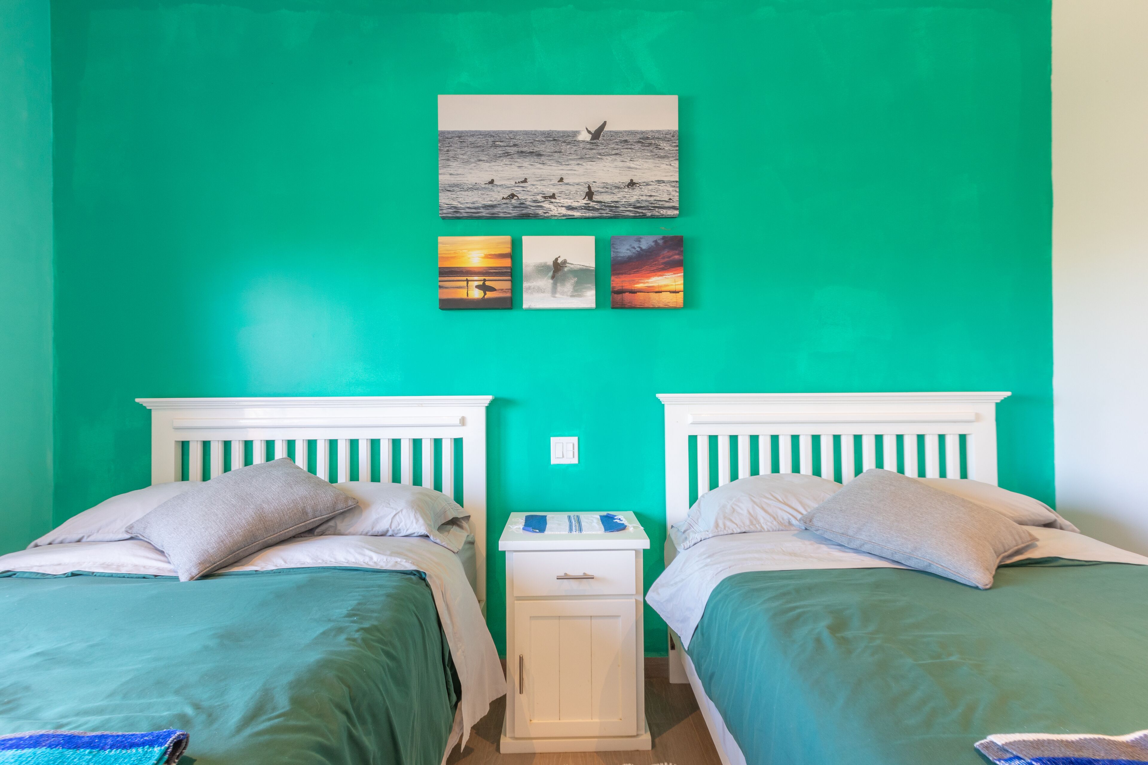 Una habitación con dos camas, paredes verde azulado y una mesita de noche pequeña con una lámpara.