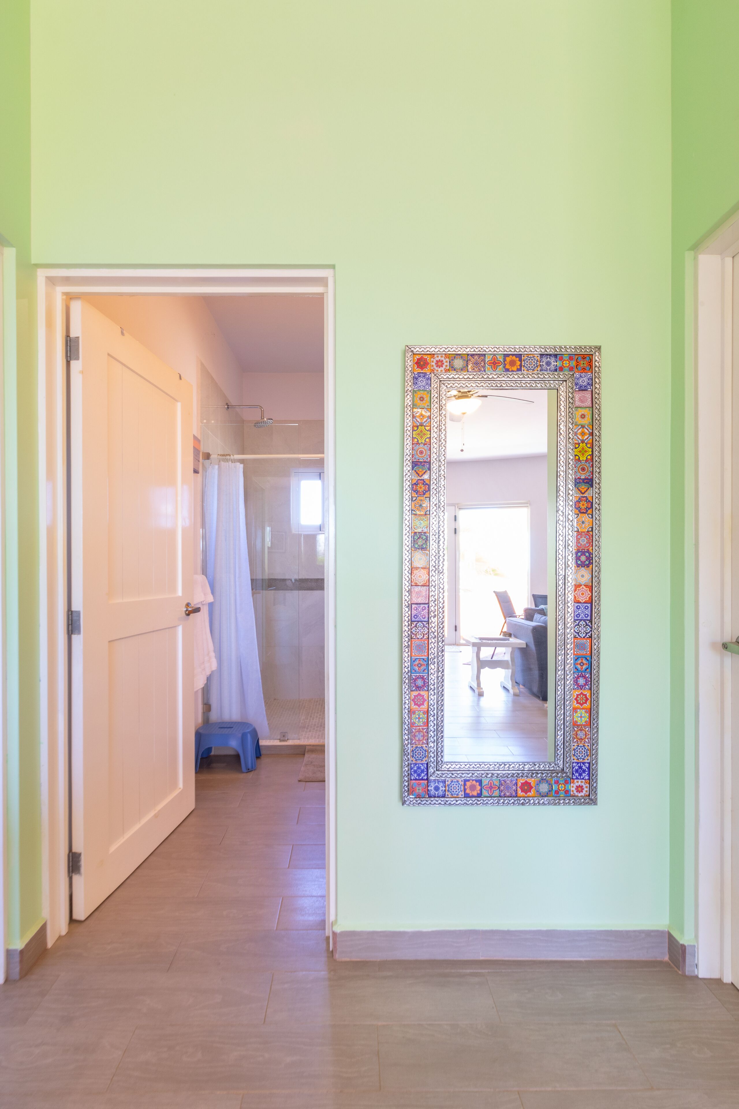 Un pasillo con zona de ducha, un espejo de marco colorido y una puerta que da a otra habitación.