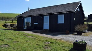 A black wooden building with a sloped roof, a front door, and a small porch area.