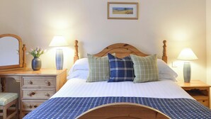 A neatly made bed with a wooden headboard, two bedside tables with lamps, a mirror, a vase with flowers, and a framed picture on the wall.