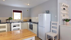 A compact kitchen with a wooden table, white cabinetry, a built-in oven, and a white refrigerator.